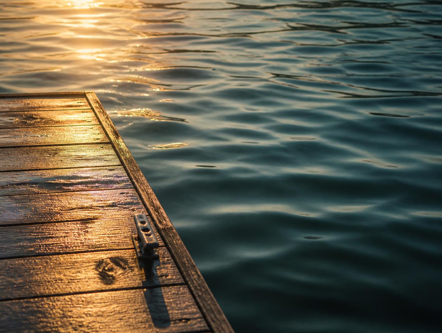 Sunlit wooden dock edge meeting rippling lake water